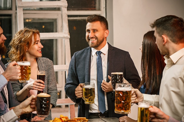 Grupo de amigos disfrutando de bebidas por la noche con cerveza en la mesa de madera