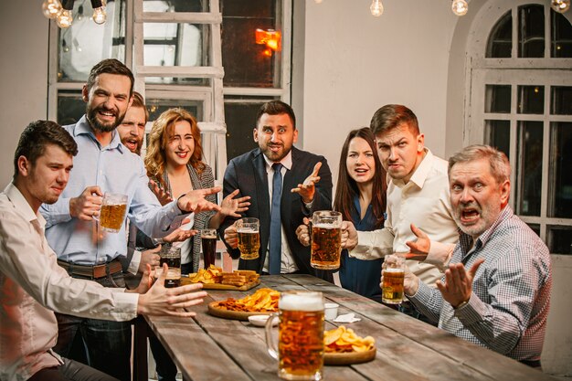 Grupo de amigos disfrutando de bebidas por la noche con cerveza en la mesa de madera