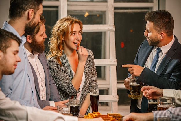 Grupo de amigos disfrutando de bebidas por la noche con cerveza en la mesa de madera