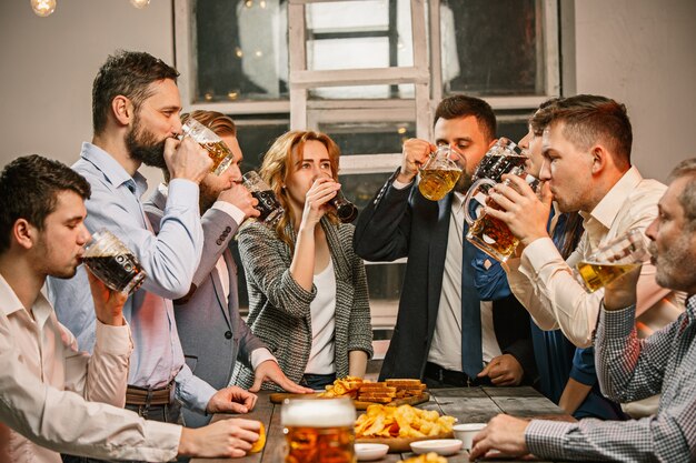 Grupo de amigos disfrutando de bebidas por la noche con cerveza en la mesa de madera
