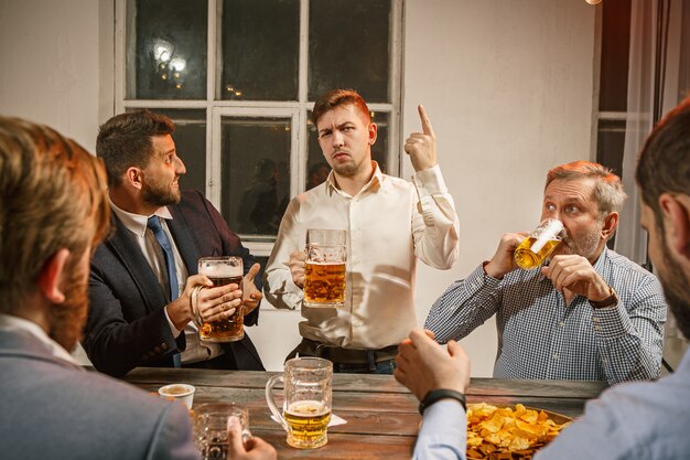 Grupo de amigos disfrutando de bebidas por la noche con cerveza en la mesa de madera