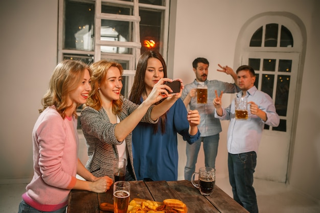 Grupo de amigos disfrutando de bebidas por la noche con cerveza en la mesa de madera