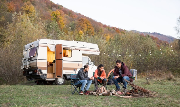 Grupo de amigos disfrutando de su tiempo juntos en las montañas. Amigos camping y autocaravana retro en el fondo.