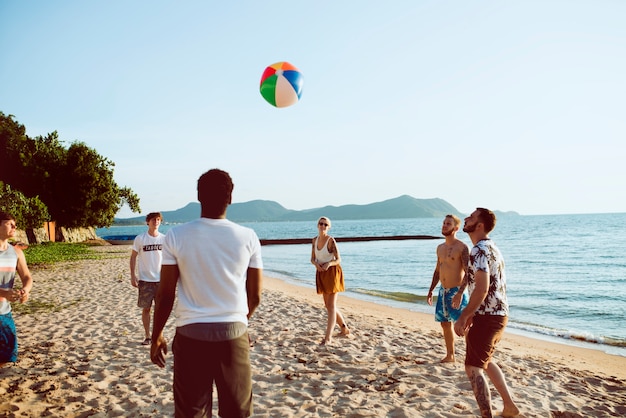 Grupo de amigos diversos que juegan el balón de playa junto