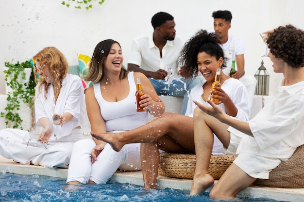 Grupo de amigos divirtiéndose durante una fiesta blanca con bebidas junto a la piscina