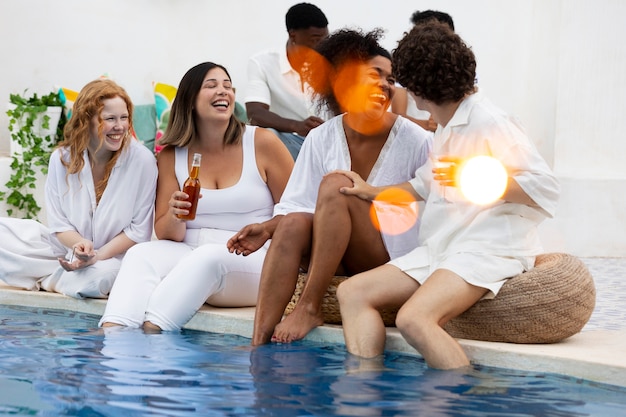 Grupo de amigos divirtiéndose durante una fiesta blanca con bebidas junto a la piscina