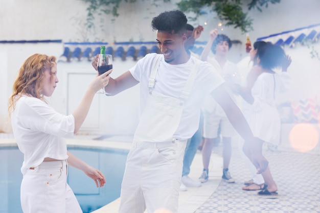 Foto gratuita grupo de amigos divirtiéndose durante una fiesta blanca con bebidas junto a la piscina