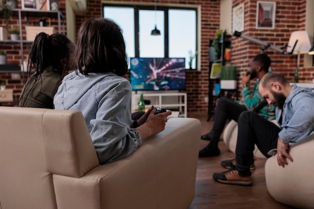 Grupo de amigos divirtiéndose con videojuegos de disparos en la televisión, usando la consola para jugar en la televisión. Jugar juegos de disparos en reuniones sociales con personas, disfrutar de actividades de ocio y juegos.