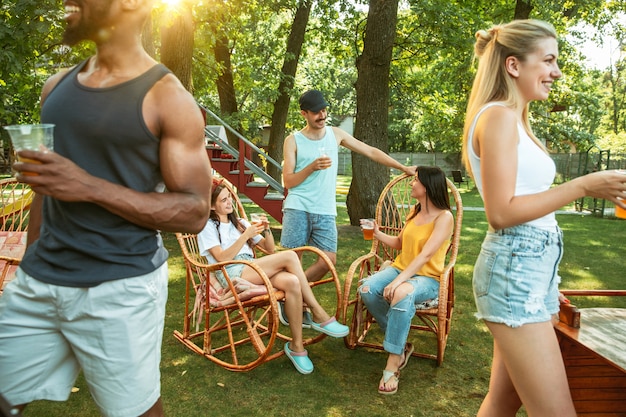 Grupo de amigos felices con cerveza y fiesta de barbacoa en un día soleado. Descansar juntos al aire libre en un claro del bosque o en el patio trasero