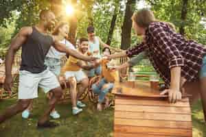 Foto gratuita grupo de amigos felices con cerveza y fiesta de barbacoa en un día soleado. descansar juntos al aire libre en un claro del bosque o en el patio trasero