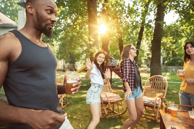 Grupo de amigos felices con cerveza y fiesta de barbacoa en un día soleado. Descansar juntos al aire libre en un claro del bosque o en el patio trasero