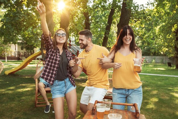 Grupo de amigos felices con cerveza y fiesta de barbacoa en un día soleado. Descansar juntos al aire libre en un claro del bosque o en el patio trasero