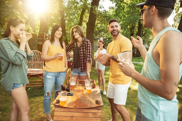 Grupo de amigos felices con cerveza y fiesta de barbacoa en un día soleado. descansar juntos al aire libre en un claro del bosque o en el patio trasero