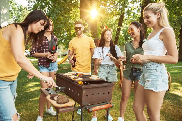 Grupo de amigos felices con cerveza y fiesta de barbacoa en un día soleado. Descansar juntos al aire libre en un claro del bosque o en el patio trasero