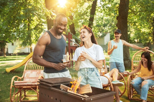 Grupo de amigos felices con cerveza y fiesta de barbacoa en un día soleado.