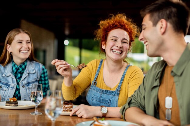 Grupo de amigos felices divirtiéndose mientras comen pastel en un café