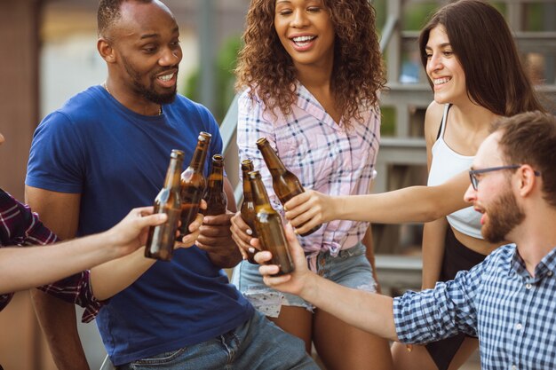 Grupo de amigos felices con fiesta de cerveza en día de verano. Descansar juntos al aire libre, celebrar y relajarse, reír. Estilo de vida de verano, concepto de amistad.