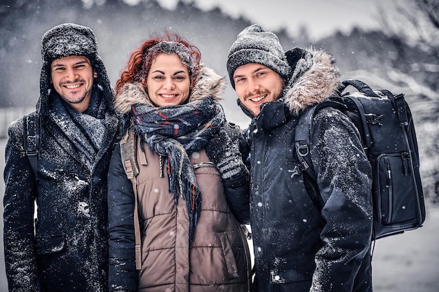 Un grupo de amigos felices se paran uno al lado del otro y miran la cámara en medio de un bosque nevado