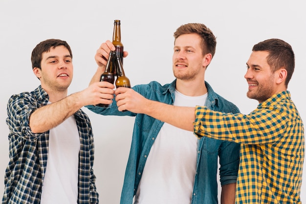 Grupo de amigos felices tostado botellas de cerveza contra el fondo blanco