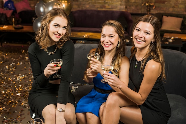 Grupo de amigos femeninos atractivos sonrientes con un vidrio de bebidas en partido
