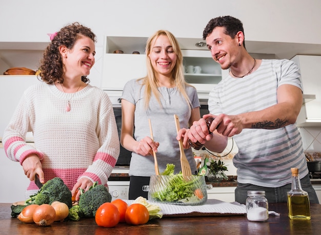 Grupo de amigos juntos haciendo ensalada de verduras frescas en la cocina
