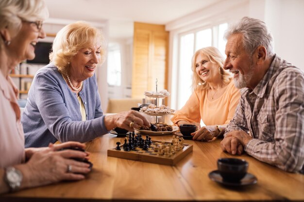 Grupo de amigos maduros disfrutando mientras juegan al ajedrez durante la hora del café en casa