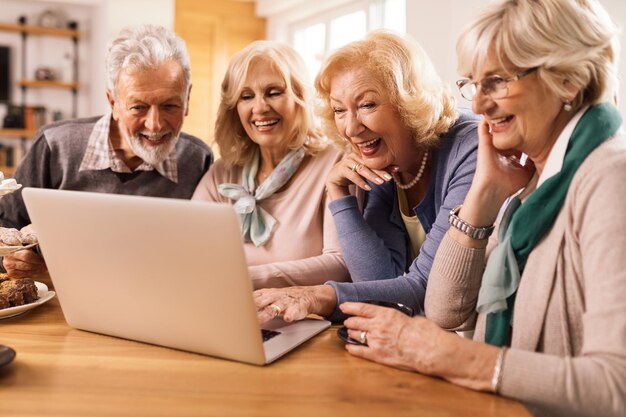 Grupo de amigos maduros felices divirtiéndose mientras navegan por la red en una computadora en casa