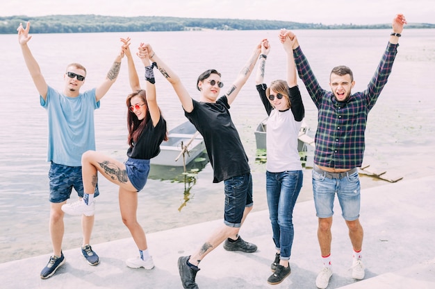 Foto gratuita grupo de amigos de pie cerca del lago levantando sus manos