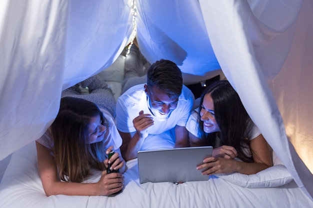 Grupo de amigos que mienten en la cama que se ríe mientras que mira en la computadora portátil