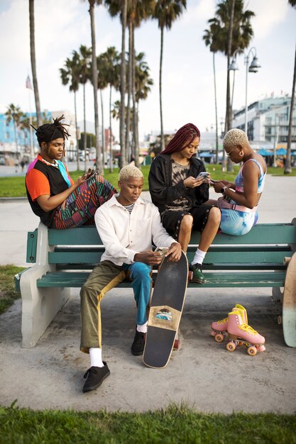 Grupo de amigos que usan teléfonos inteligentes mientras están sentados en un banco afuera en el parque
