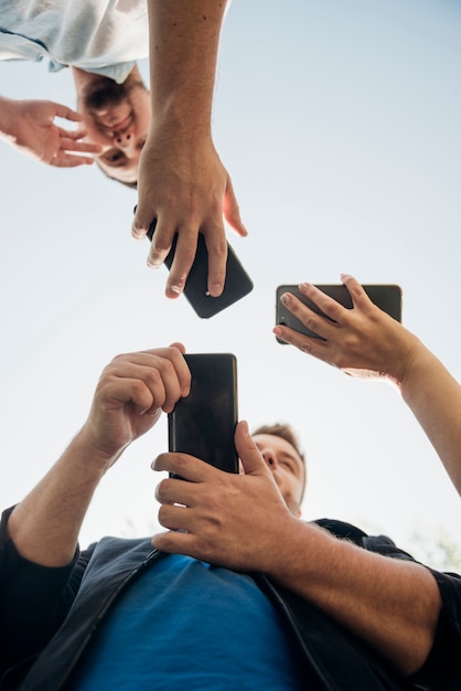 Grupo de amigos relajándose con teléfonos inteligentes afuera