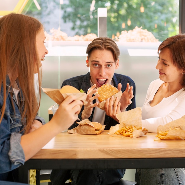 Grupo de amigos en el restaurante de comida rápida comiendo hamburguesas con queso