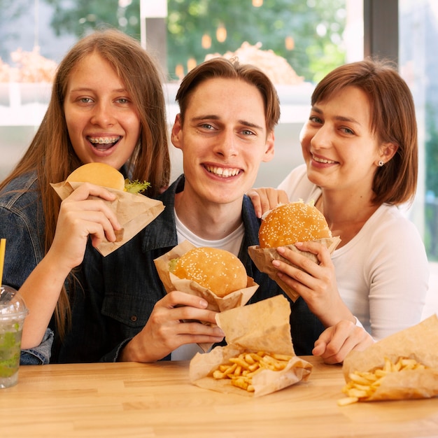 Grupo de amigos en el restaurante de comida rápida comiendo hamburguesas