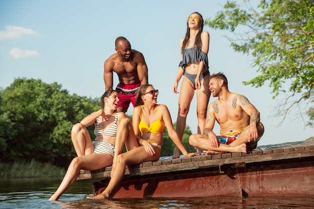 Foto gratuita grupo de amigos salpicando agua y riendo en el muelle en el río