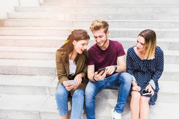 Grupo de amigos sentados en la escalera mirando la pantalla del teléfono móvil