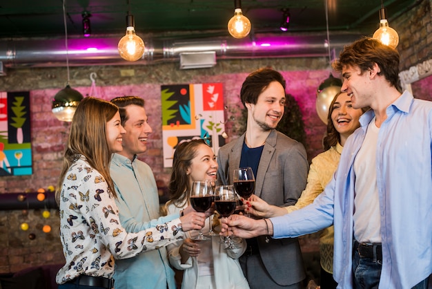 Grupo de amigos sonrientes masculinos y femeninos que tuestan el vino en club en la noche