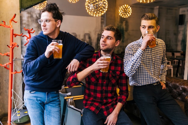 Foto gratuita grupo de amigos sosteniendo los vasos de cerveza mirando a otro lado