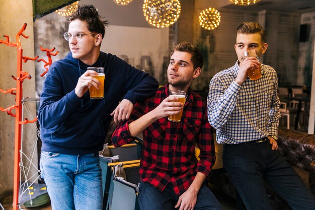 Grupo de amigos sosteniendo los vasos de cerveza mirando a otro lado