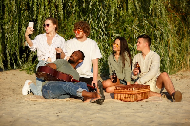 Foto gratuita grupo de amigos tintineo de vasos de cerveza durante un picnic en la playa