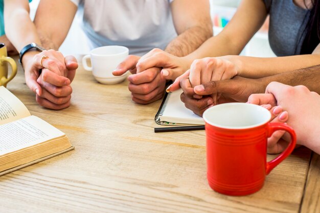 Grupo de amigos tomados de la mano sobre la mesa con libros y tazas de bebida