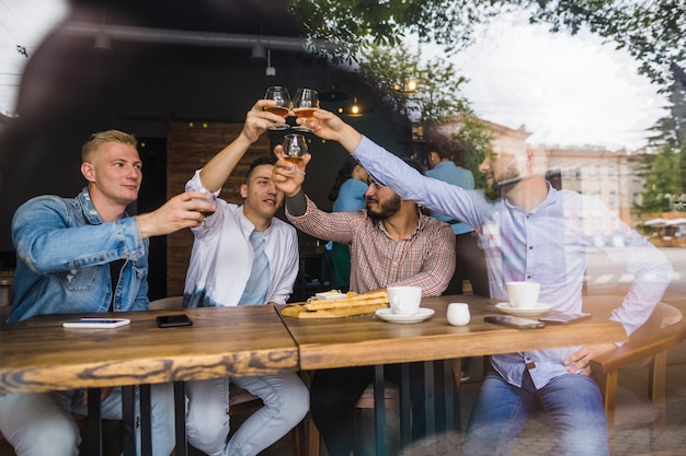 Foto gratuita grupo de amigos varones levantando brindis en el restaurante