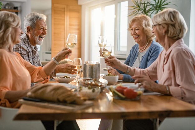 Grupo de ancianos felices divirtiéndose mientras brindan con copas de vino durante el almuerzo en casa