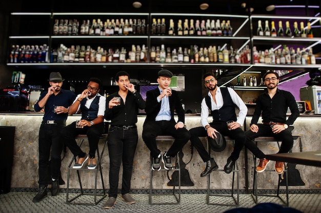 Foto gratuita grupo de apuestos gánsteres retro bien vestidos pasan tiempo en el club bebiendo whisky en el mostrador del bar fiesta multiétnica de solteros mafiosos en el restaurante