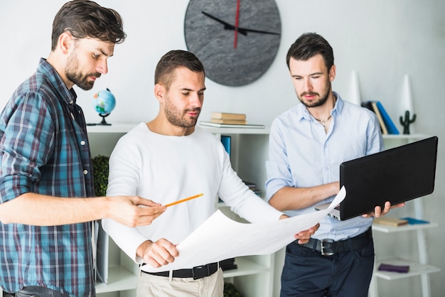 Grupo de arquitecto masculino que usa la computadora portátil mientras que mira el modelo