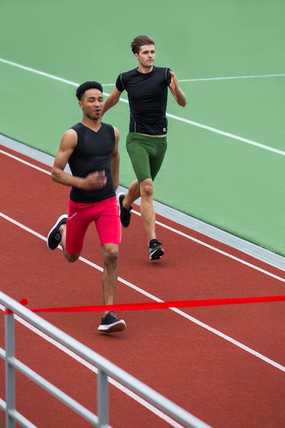 Grupo de atletas hombres correr en pista de atletismo al aire libre