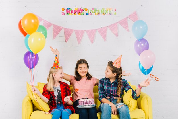 Grupo de chicas sentadas en el sofá con pastel de cumpleaños