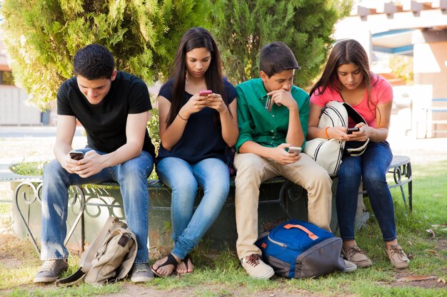 Grupo de chicos y chicas adolescentes ignorándose unos a otros mientras usan sus teléfonos celulares en la escuela