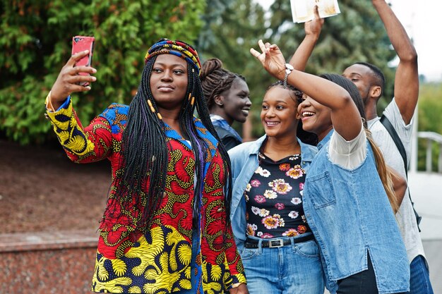 Grupo de cinco estudiantes universitarios africanos que pasan tiempo juntos en el campus en el patio de la universidad Amigos afro negros haciendo selfie por teléfono Tema educativo