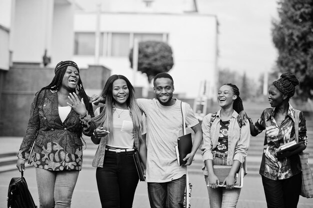 Grupo de cinco estudiantes universitarios africanos que pasan tiempo juntos en el campus en el patio de la universidad Amigos afro negros que estudian el tema de la educación