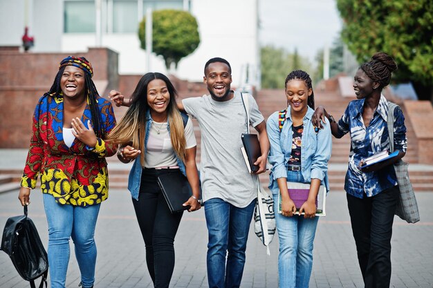 Grupo de cinco estudiantes universitarios africanos que pasan tiempo juntos en el campus en el patio de la universidad Amigos afro negros que estudian el tema de la educación